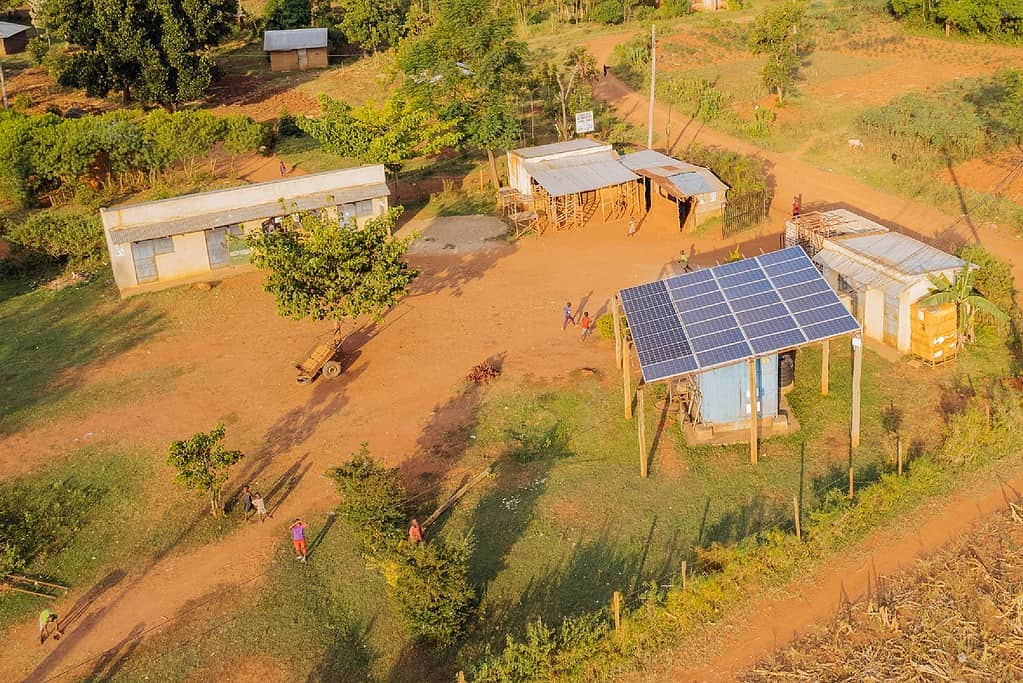 A rural area with solar panels on rooftops, small buildings, and surrounding greenery.