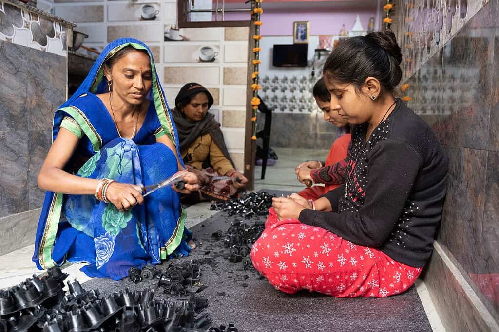Women sit on the floor in a kitchen cutting out plastic plugs from molds