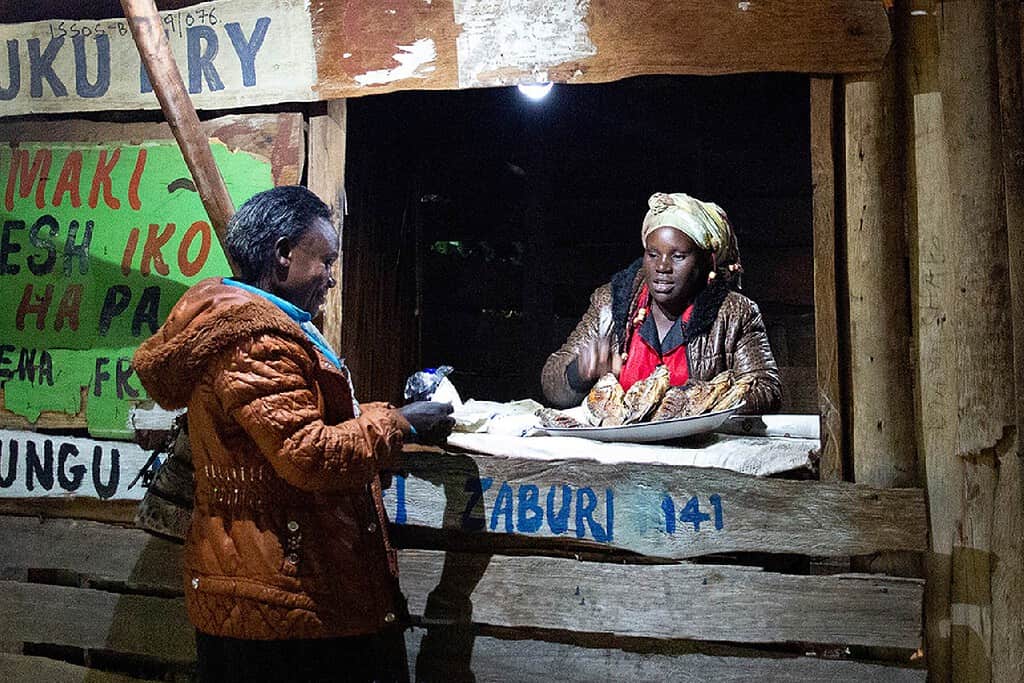 Woman buys fried fish from a shop using solar powered lights