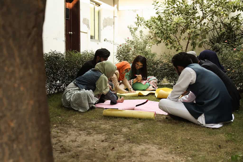 A group of students work on a poster in the garden of a Pakistani school building