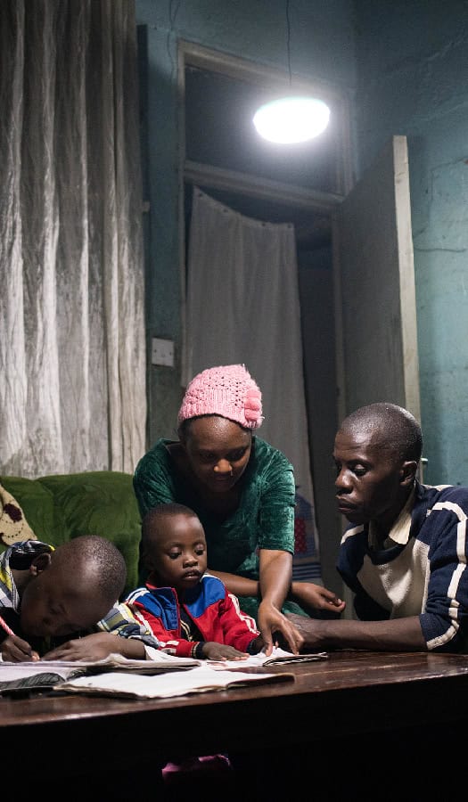 Family sits around table helping children with their homework under solar-powered lighting