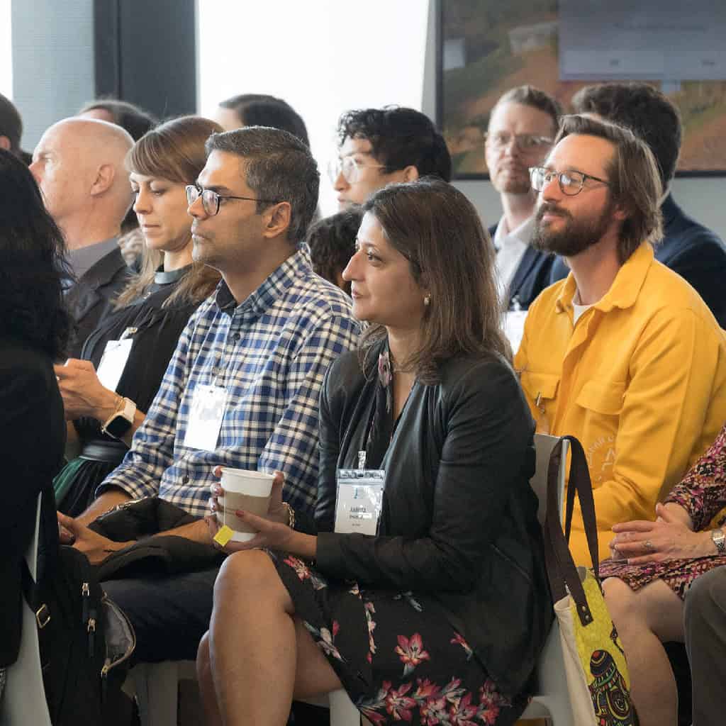 A group of people seated, attentively listening at an event, some with name tags.
