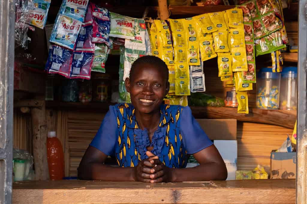 A smiling person stands behind a kiosk counter with various packaged goods, representing small business entrepreneurship.
