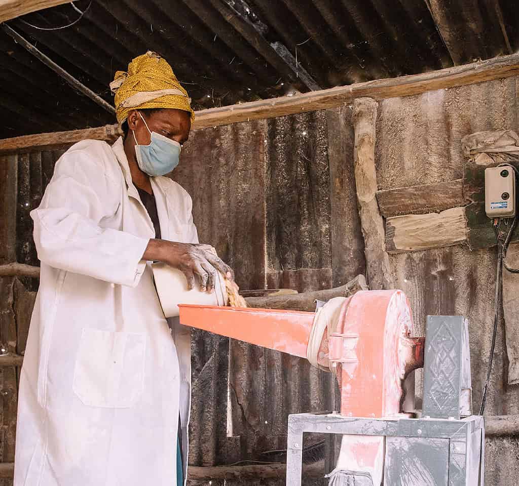 Woman pours in grain for milling into flour in East African shed