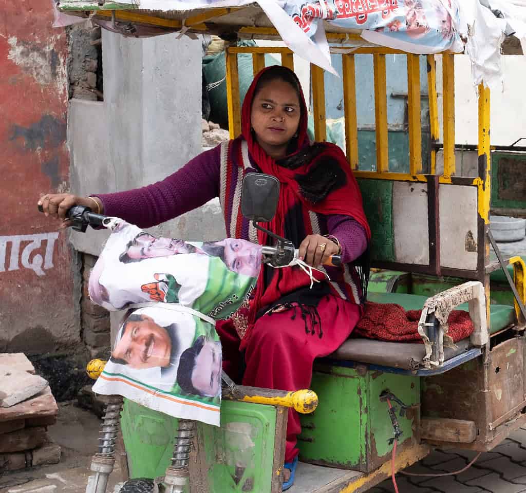 Woman driving a rickshaw, motorbike, through a neighborhood street in India