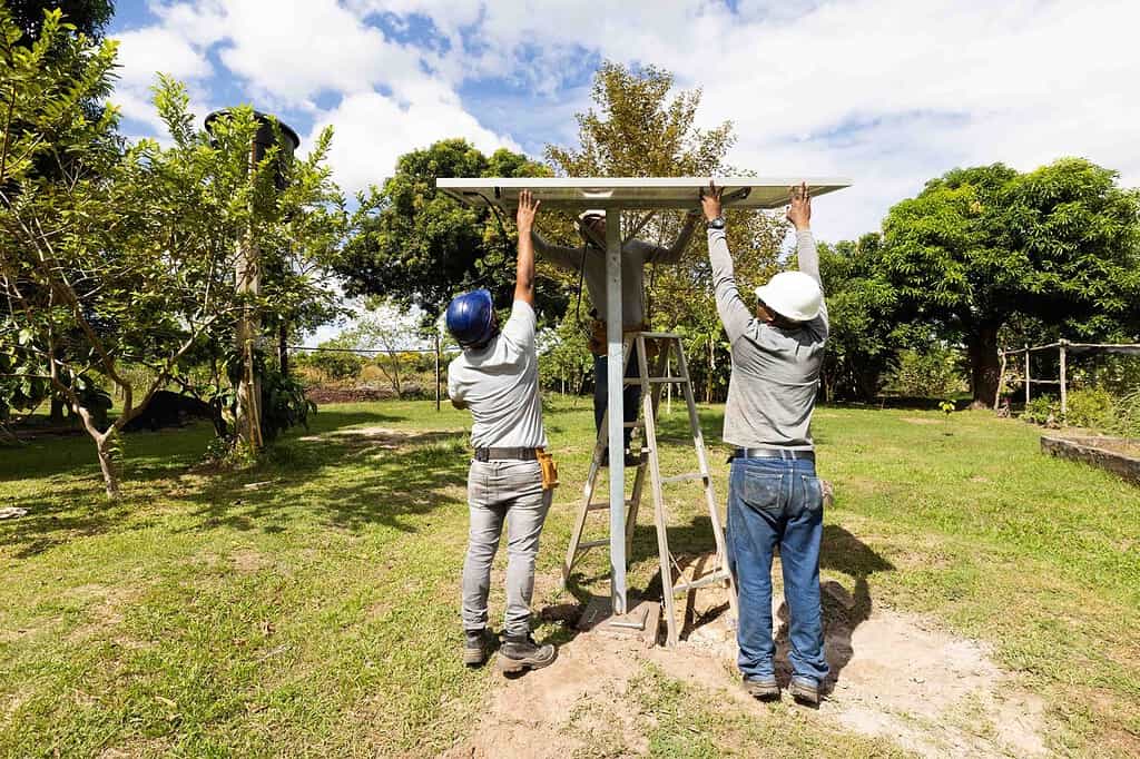 Three technicians carefully install solar panel in a yard at a rural Colombian home