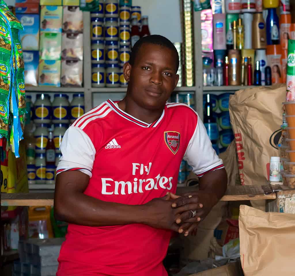 Shop owners stands in small shop newly lit by solar powered lights