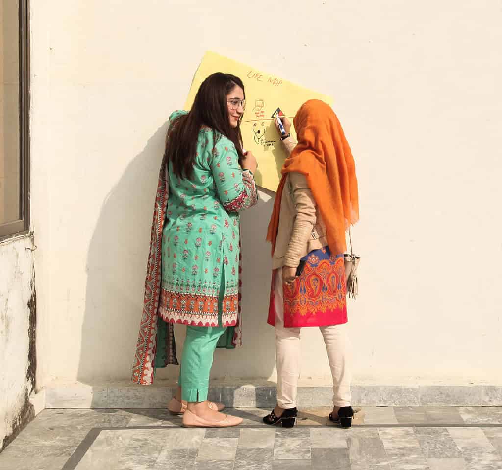 Two women write on large poster while using a wall as writing support