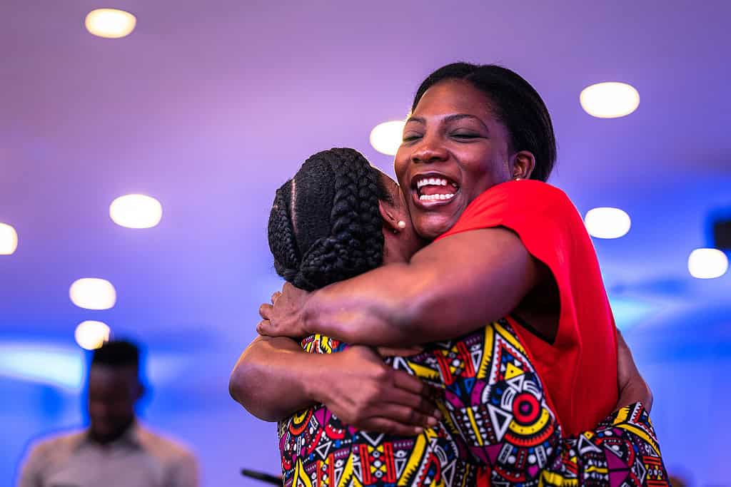 Two women happily hug at a speaking event