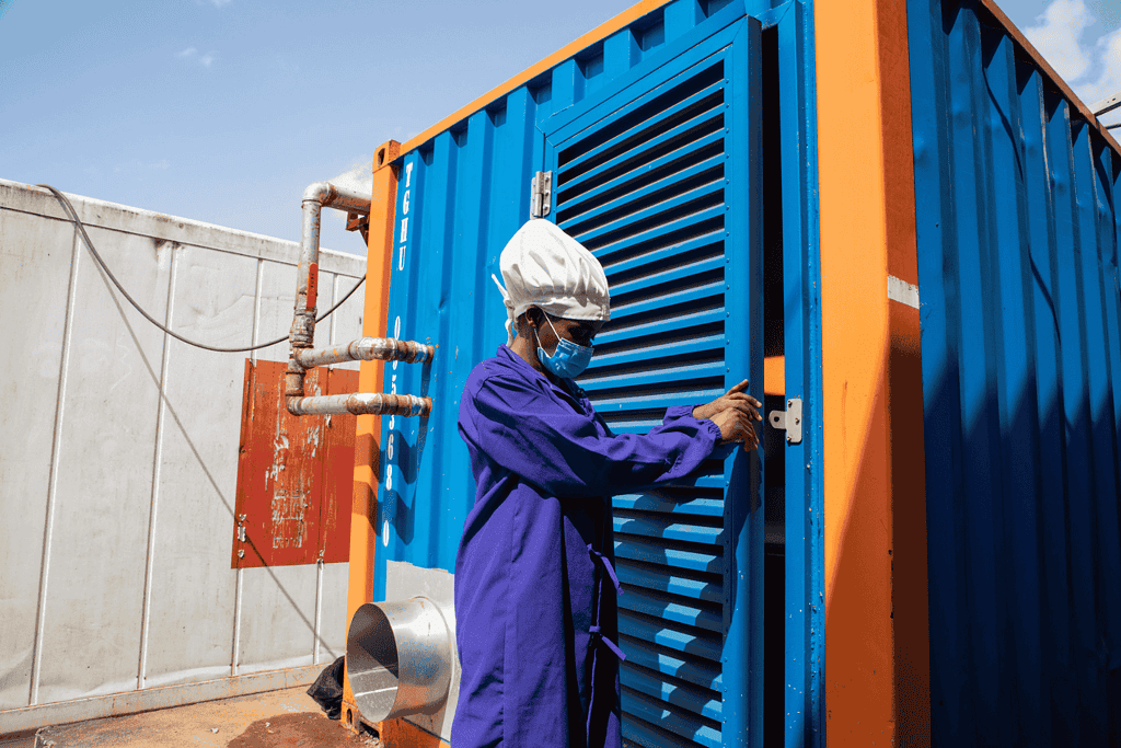 A person in protective clothing is interacting with a shipping container structure.
