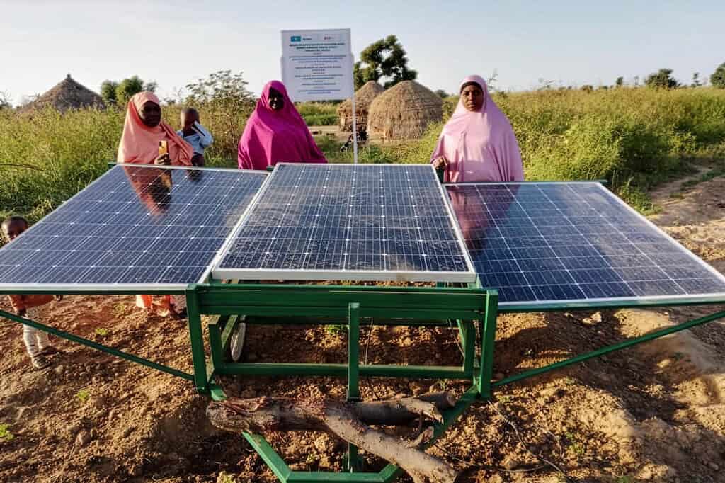 Women stand next to solar panels in field