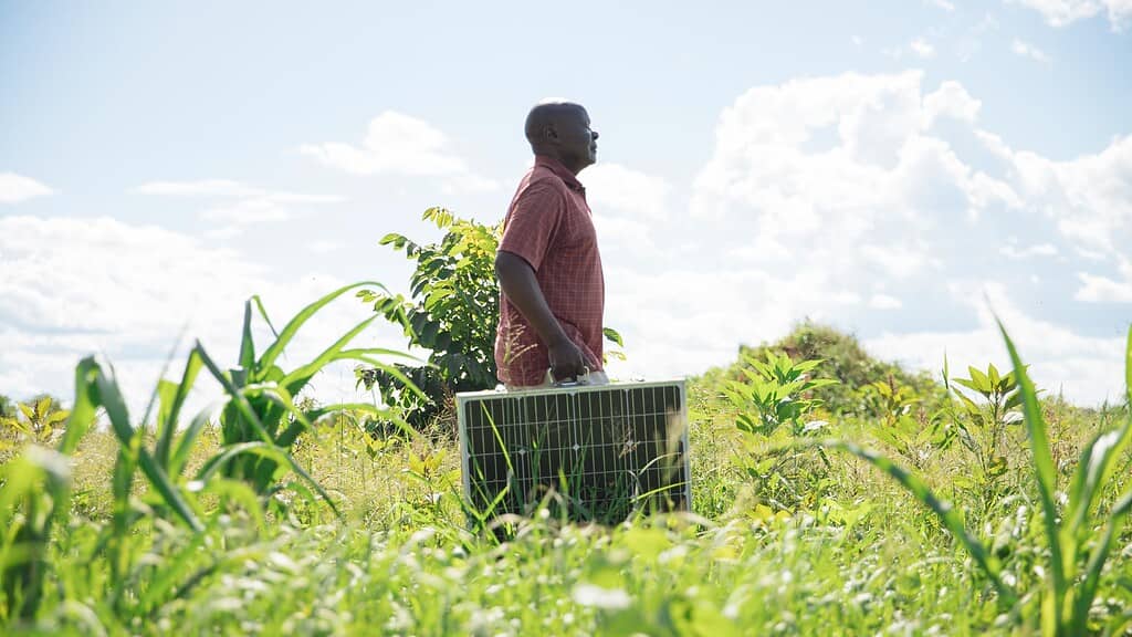 Farmer walks through field with a portable solar panel. Photo courtesy of Tulimasolar (Simusolar) and Peter Irungu